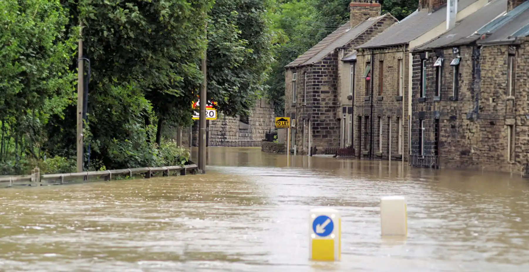 Flooded residential street with brown water submerging road signs and reaching building doorsteps.