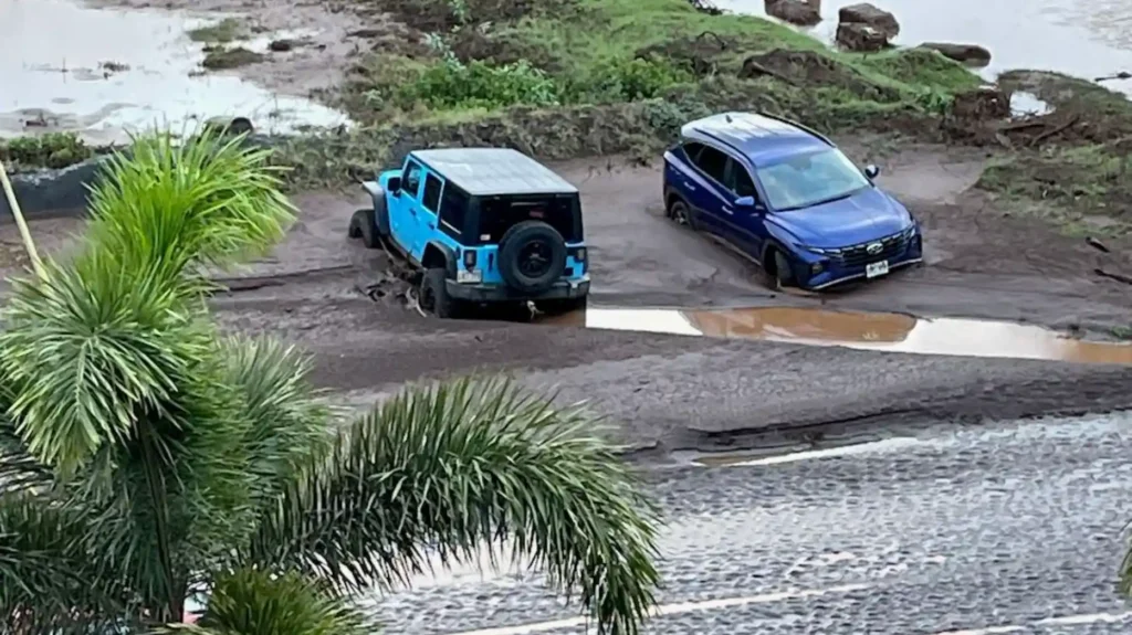 Two vehicles stranded in deep mud near floodwater, surrounded by debris and soaked ground.